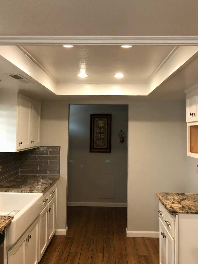 Bright kitchen corner transformation showing newly painted white cabinetry, grey wood-look flooring, and subway tile backsplash