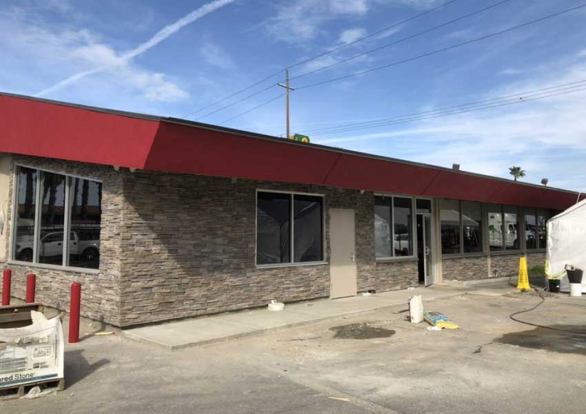 commercial building with a finished grey paint job on the upper fascia and red paint on the far right section, still showing some construction materials and equipment outside
