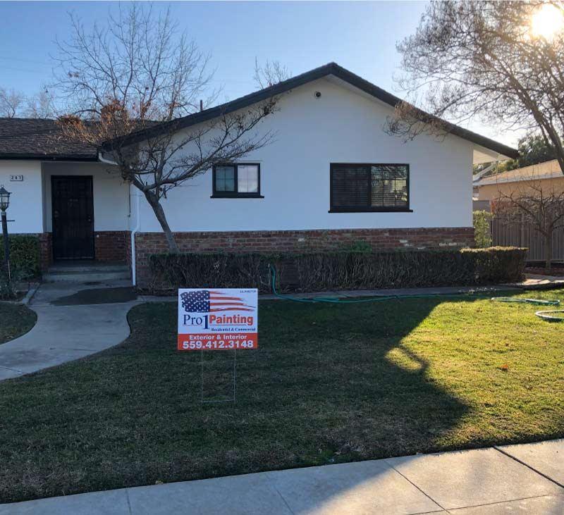 Modern residential exterior makeover featuring bright white stucco, black window trim, and red brick wainscoting