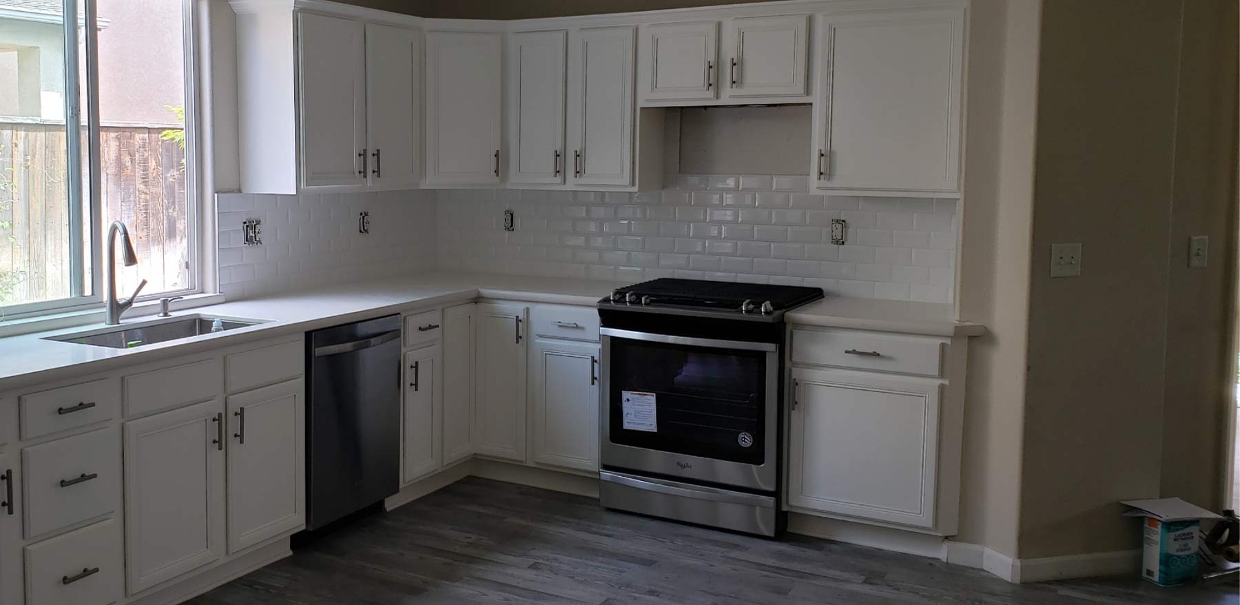 Freshly refinished white kitchen cabinets with modern subway tile backsplash and stainless steel gas range after professional painting