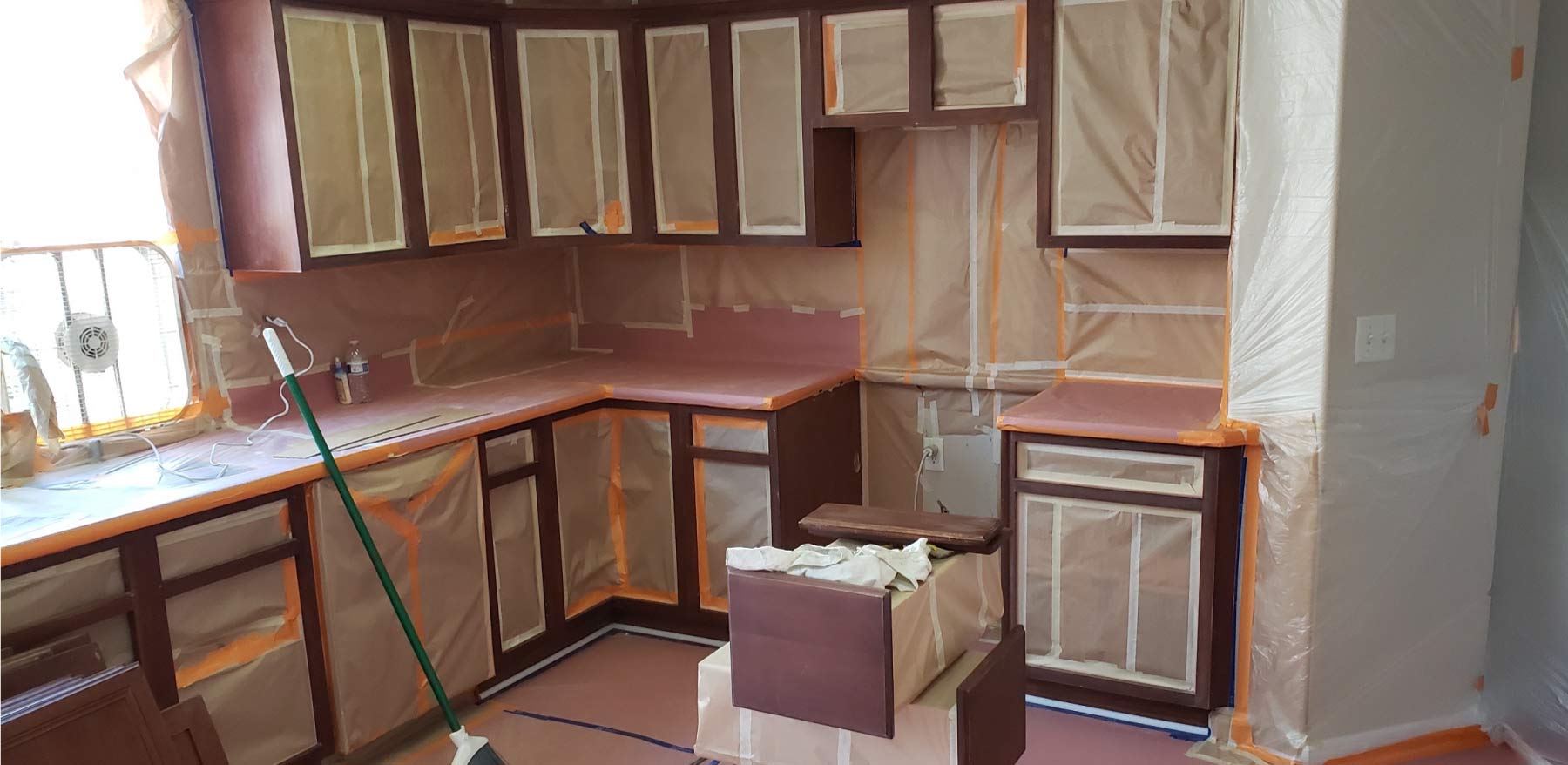 Kitchen cabinets extensively masked with brown paper and tape in preparation for professional spray painting and refinishing services.