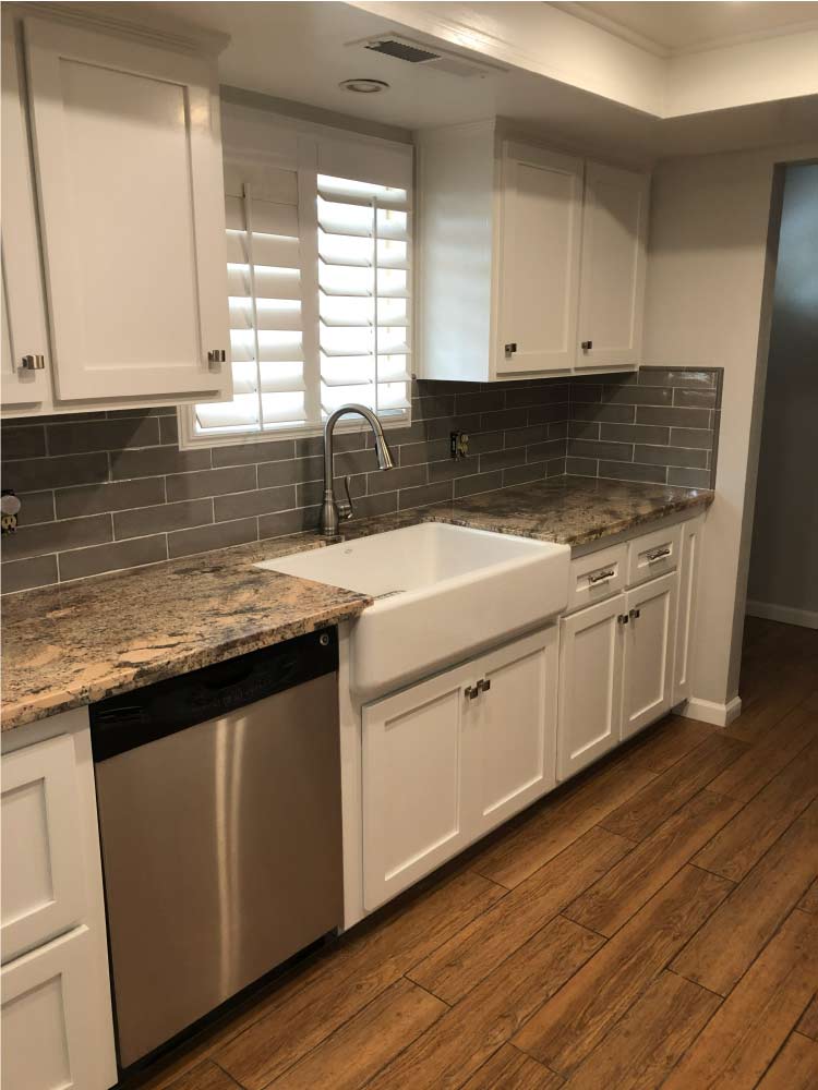 Renovated kitchen featuring freshly painted white shaker cabinets, farmhouse sink, and grey subway tile backsplash in Fresno CA