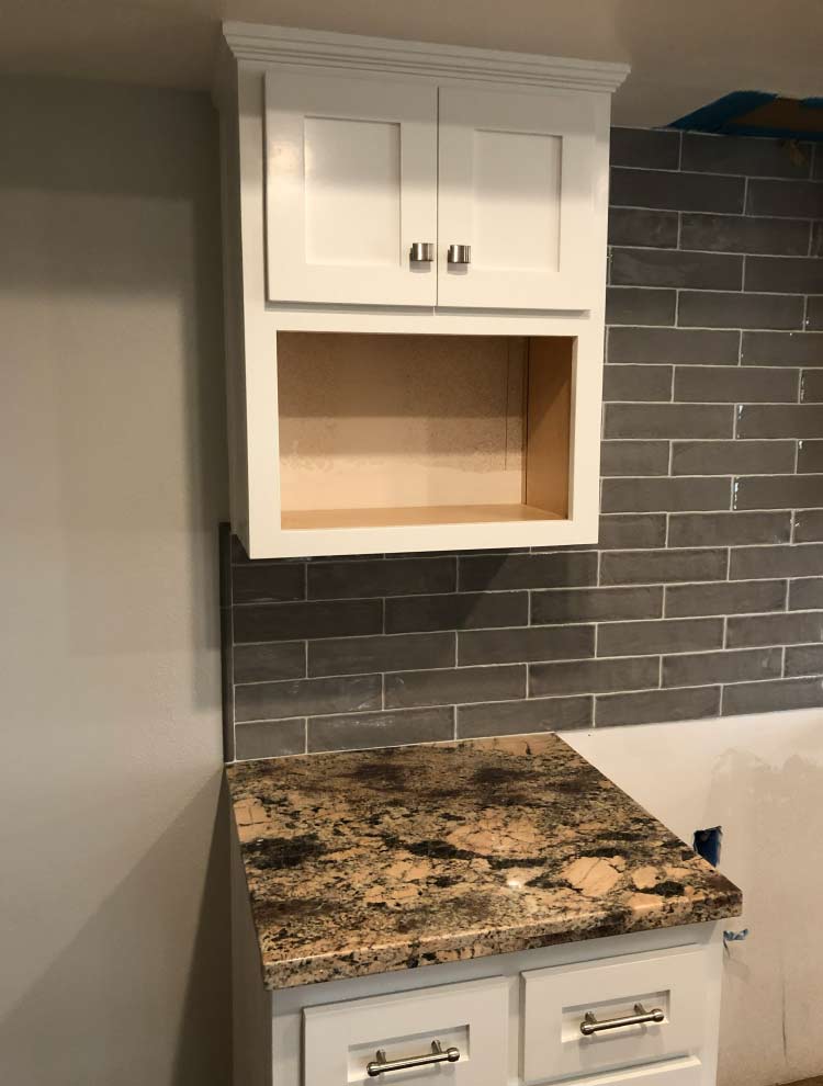 Close-up of newly painted upper white kitchen cabinets with modern brush nickel hardware and dark grey tile backsplash