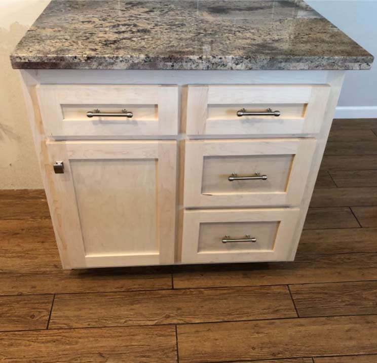 Close-up of unfinished raw wood kitchen island cabinets with granite countertops before professional cabinet refinishing and painting services.