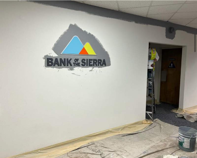 Commercial painters using drop cloths and masking to protect office flooring during interior wall painting at Bank of the Sierra